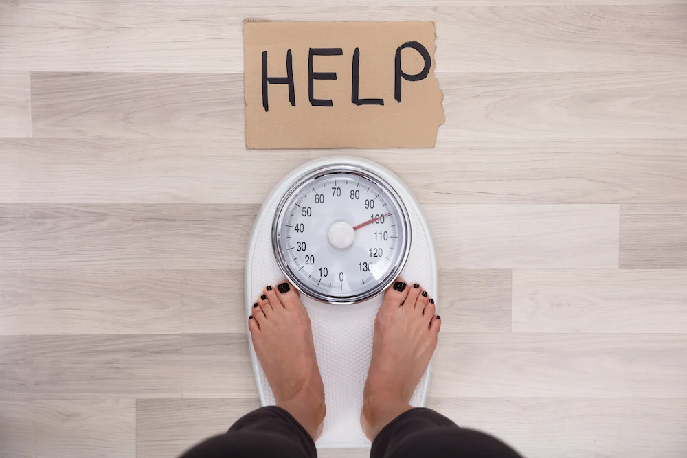 Una donna in piedi sulla bilancia che indica un eccesso di peso e chiede aiuto. Ma si tratta di sovrappeso o di un segnale di carenze micronutrienti?